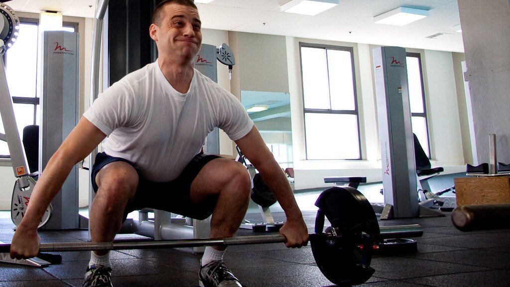 A man in a gym lifting a barbell from the floor